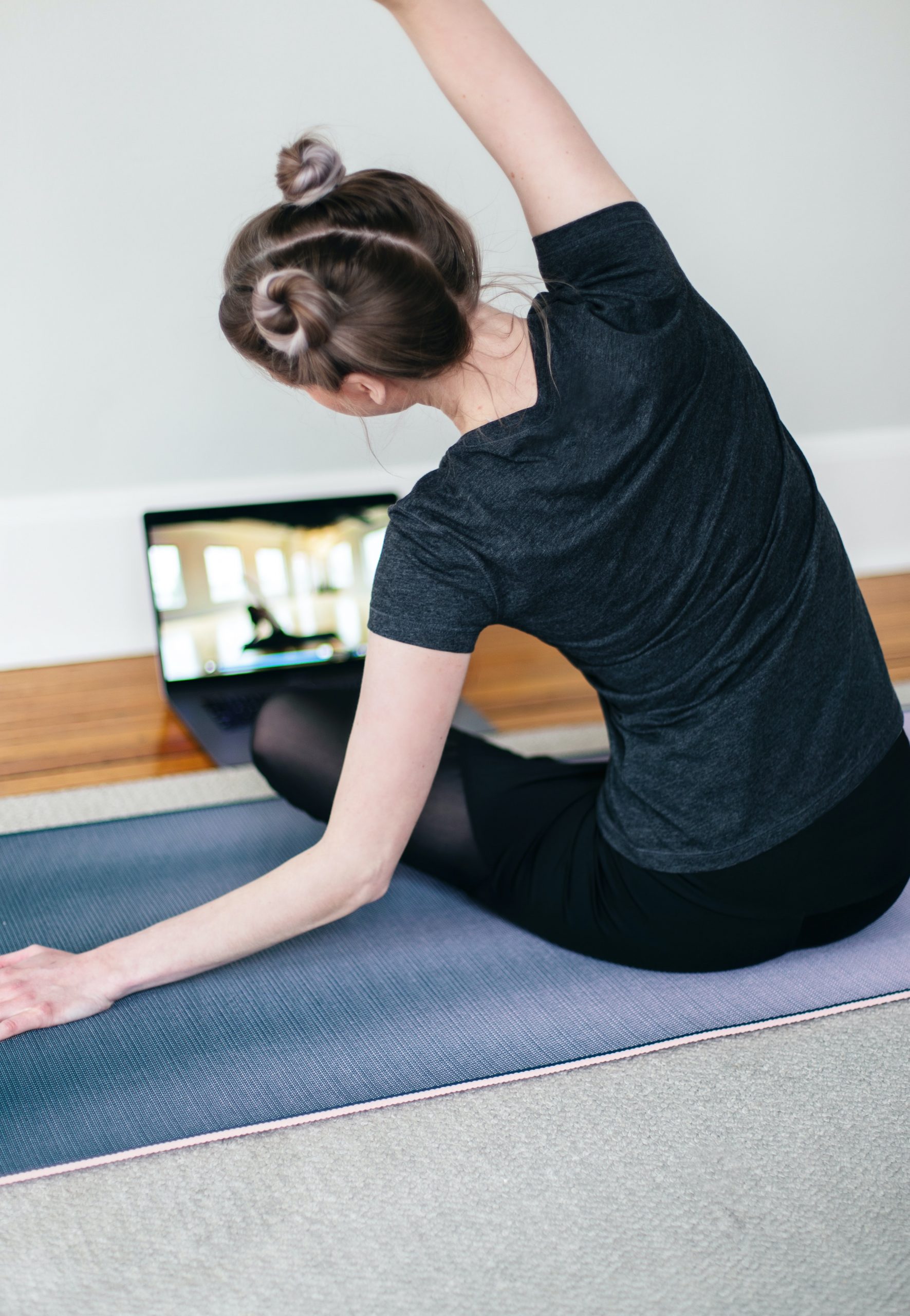 Frau übt vor ihrem Laptop auf dem Boden sitzend Yoga
